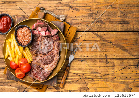 A juicy Grilled Chuck eye roll steak and garnish with french fry on a plate. wooden background. top view A juicy Grilled Chuck eye roll steak and garnish with french fry on a plate. wooden background. top view 129615674