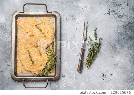Cooking of Raw breaded Wiener Schnitzel steak in steel tray. gray background. top view 129615676