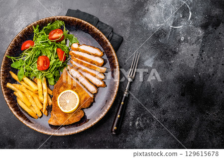 Roast viennese schnitzel steak, breaded meat with salad and french fry on a plate. black background. top view Roast viennese schnitzel steak, breaded meat with salad and french fry on a plate. black background. top view 129615678