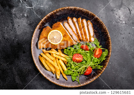 Roast viennese schnitzel steak, breaded meat with salad and french fry on a plate. black background. top view 129615681