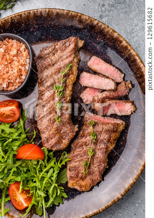 BBQ Grilled skirt or machete Steak, beef meat on a plate with salad. grey background. top view BBQ Grilled skirt or machete Steak, beef meat on a plate with salad. grey background. top view 129615682