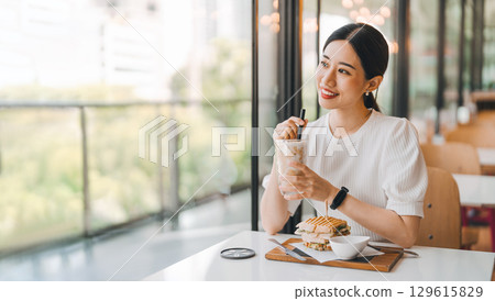 Happy asian woman healthy eating breakfast sandwich at cafe sitting near window indoors on day Happy asian woman healthy eating breakfast sandwich at cafe sitting near window indoors on day 129615829