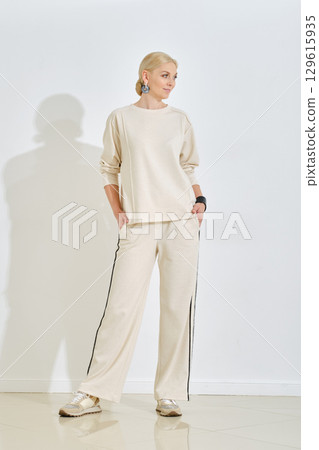 Fashionable model showcases neutral outfit in minimalist studio environment during daylight 129615935