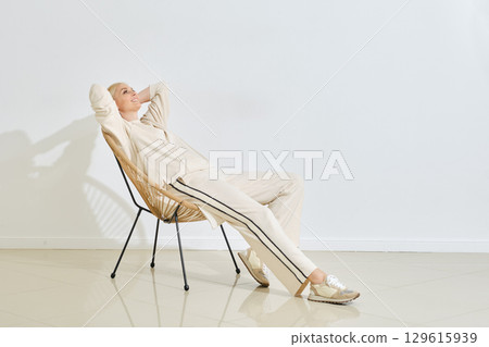 Relaxing in a modern chair, a woman enjoys a quiet moment in a minimalist indoor space 129615939