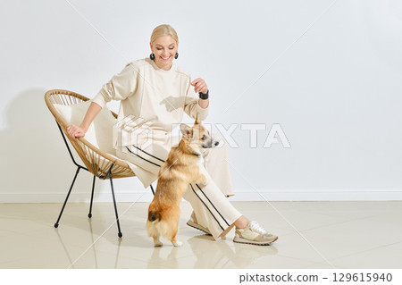 Happy woman enjoys time with corgi in modern interior setting during daytime Happy woman enjoys time with corgi in modern interior setting during daytime 129615940