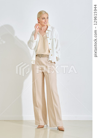 Stylish woman showcases chic outfit in neutral tones in a minimalist setting 129615944
