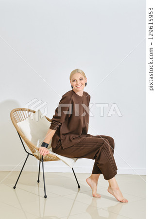 Woman seated in a stylish chair wearing comfortable brown loungewear in a bright interior space Woman seated in a stylish chair wearing comfortable brown loungewear in a bright interior space 129615953