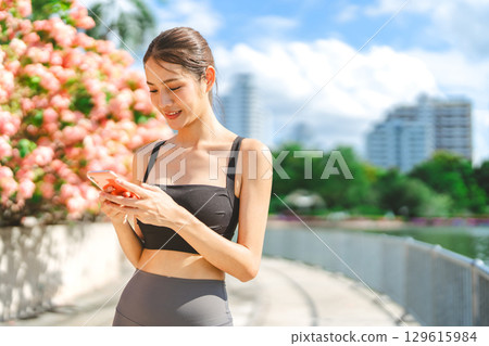 Young adult asian sport woman using smartphone social media rest from running at outdoors Young adult asian sport woman using smartphone social media rest from running at outdoors 129615984