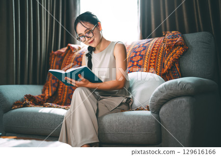 Adult asian woman reading book on sofa relax routines everyday at living room Adult asian woman reading book on sofa relax routines everyday at living room 129616166