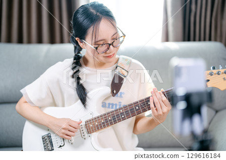 Young adult asian woman playing electric guitar music live on social media content creator at home 129616184