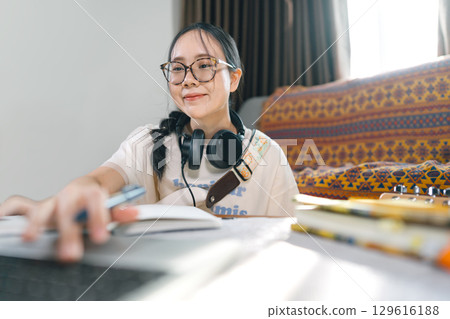 Young adult asian woman wearing headphones playing electric guitar music education online learning Young adult asian woman wearing headphones playing electric guitar music education online learning 129616188