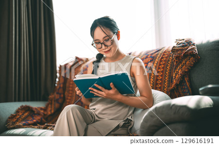 Beautiful young adult asian woman wearing eyeglasses reading book on sofa relax hobby routines Beautiful young adult asian woman wearing eyeglasses reading book on sofa relax hobby routines 129616191