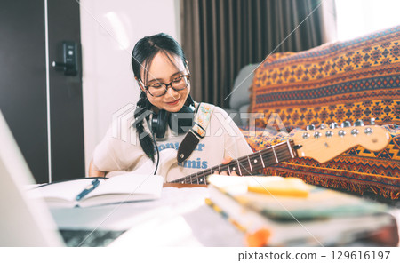 Young adult asian woman composer playing electric guitar enjoy hobby at home studio Young adult asian woman composer playing electric guitar enjoy hobby at home studio 129616197