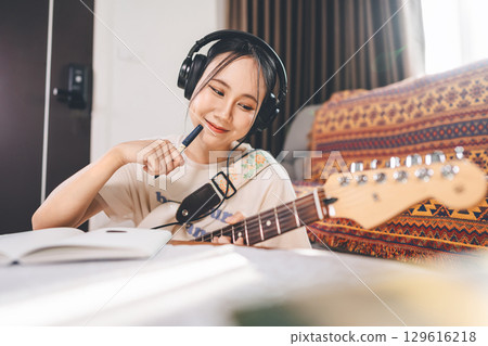 Young asian woman composer playing electric guitar wearing headphones 129616218