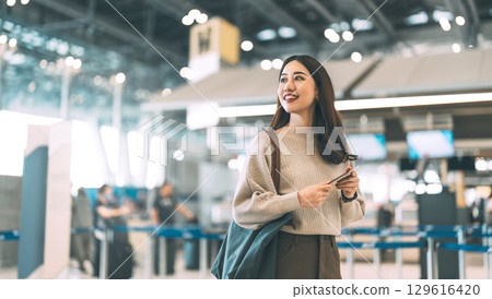 Woman passenger holding passport and boarding pass to transit at international airport terminal Woman passenger holding passport and boarding pass to transit at international airport terminal 129616420