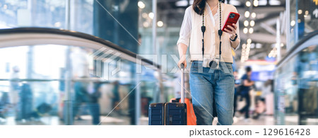 Standing passenger woman to transit with travel luggage and camera at international airport journey 129616428