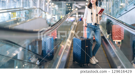 Standing passenger woman to transit with travel luggage and camera at international airport 129616429