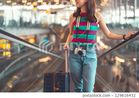 Standing passenger woman to transit with travel luggage and camera at international airport 129616432