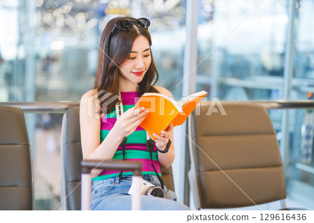 Woman reading a book at international airport terminal for waiting departure time. Woman reading a book at international airport terminal for waiting departure time. 129616436