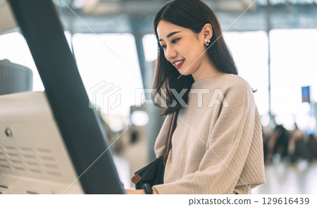 Woman passenger with travel luggage Using self service check kiosk machine at airport terminal 129616439
