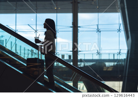Silhouette standing woman to transit with travel luggage on escalator at airport terminal 129616443