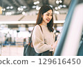 Woman passenger with travel luggage Using self service check kiosk machine at airport terminal 129616450
