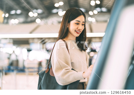 Woman passenger with travel luggage Using self service check kiosk machine at airport terminal Woman passenger with travel luggage Using self service check kiosk machine at airport terminal 129616450