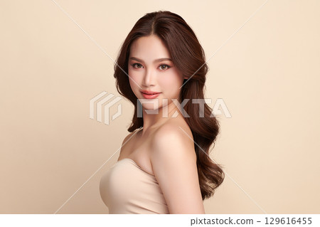 A beautiful young Asian woman with clean, fresh skin against a beige background. Skincare, facial treatment, cosmetology, beauty, and spa. An elegant portrait of an Asian woman. 129616455