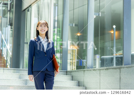 A woman in a suit walking with a file 129616842