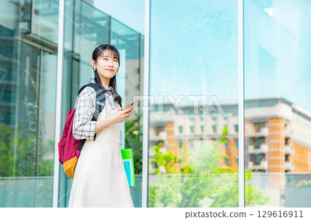 一名在校園裡操作智能手機的大學生 一名在校園裡操作智能手機的大學生 129616911