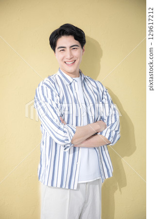 Smiling man in casual shirt with arms crossed, looking at camera, yellow background Smiling man in casual shirt with arms crossed, looking at camera, yellow background 129617212