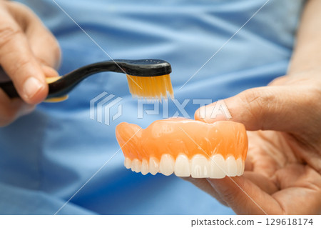 Asian senior woman patient clean teeth denture with toothbrush for chew food. Asian senior woman patient clean teeth denture with toothbrush for chew food. 129618174
