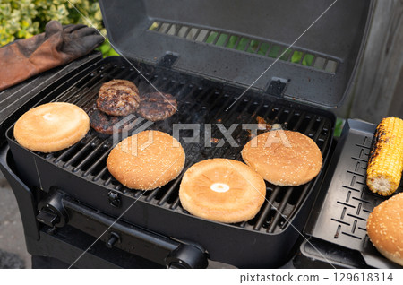 Grilling burger patties and buns outdoors with corn on summer day 129618314