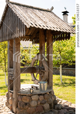 Rustic wooden water well in sunlit garden with stone base 129618357