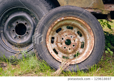 Rusty and worn vehicle wheels resting in tall grass at an abandoned location in daylight 129618697