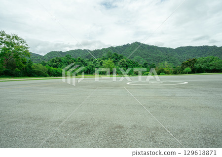 Empty helicopter landing pad with asphalt with green mountain forest background providing emergency medical transport access to remote wilderness areas. Helipad platform at dam infrastructure site. 129618871