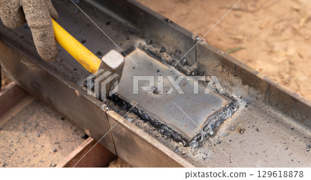 Skilled worker hammers hot metal weld in industrial workshop, capturing the artistry of metalworking, the precision of craftsmanship, and the sparks flying from the intense heat of forging. 129618878