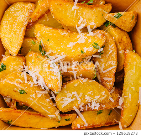 Crispy potato wedges topped with fresh herbs and cheese in a takeout box Crispy potato wedges topped with fresh herbs and cheese in a takeout box 129619278