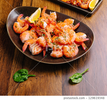 Shrimp dish served with lemon and garnished with herbs in a rustic setting 129619348
