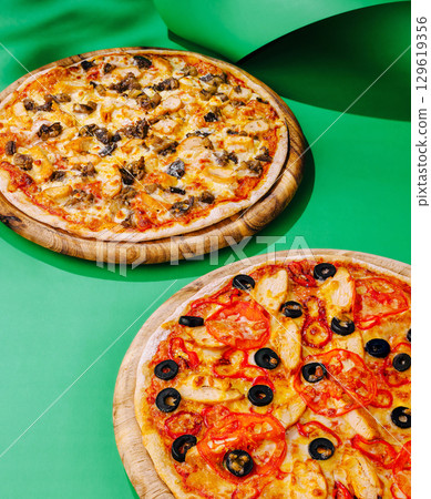 Freshly baked pizzas on wooden boards against a vibrant green backdrop Freshly baked pizzas on wooden boards against a vibrant green backdrop 129619356