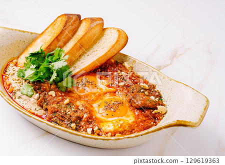 Delicious breakfast of eggs in tomato sauce with toasted bread and herbs 129619363