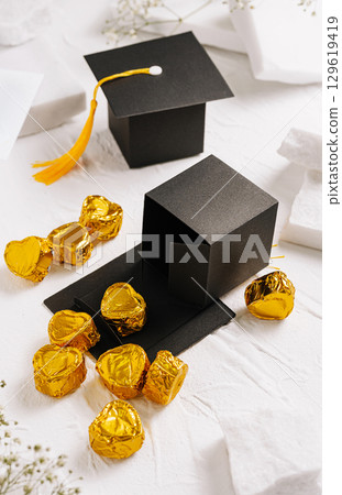 Celebration of graduation with black cap and golden candies on table Celebration of graduation with black cap and golden candies on table 129619419