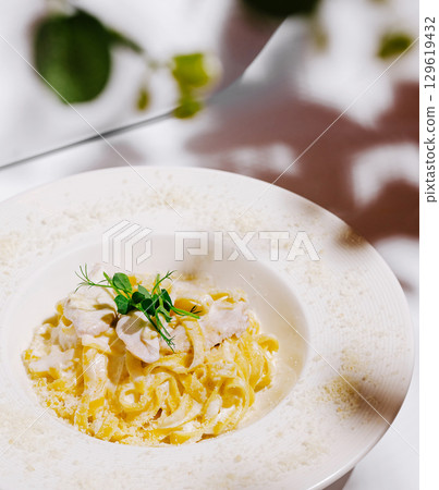 Pasta dish served in elegant white bowl with garnish and blurred background Pasta dish served in elegant white bowl with garnish and blurred background 129619432