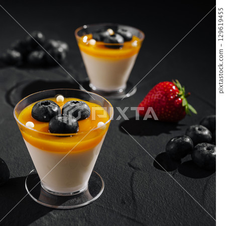 Delicious dessert cups with mango, blueberries, and strawberries on dark surface Delicious dessert cups with mango, blueberries, and strawberries on dark surface 129619455