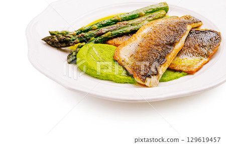 Grilled fish served with vibrant green puree and asparagus on a plate 129619457