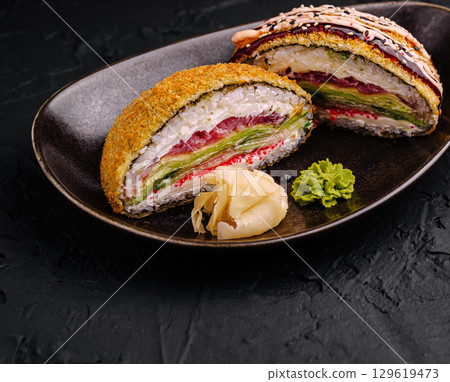 Unique layered sushi roll served on a dark plate with condiments Unique layered sushi roll served on a dark plate with condiments 129619473