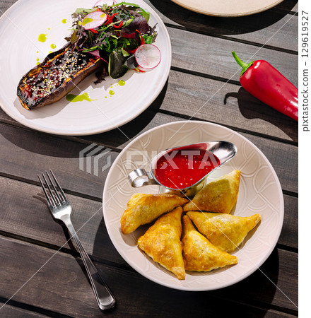 Samosas served with red sauce and grilled eggplant with salad garnish Samosas served with red sauce and grilled eggplant with salad garnish 129619527