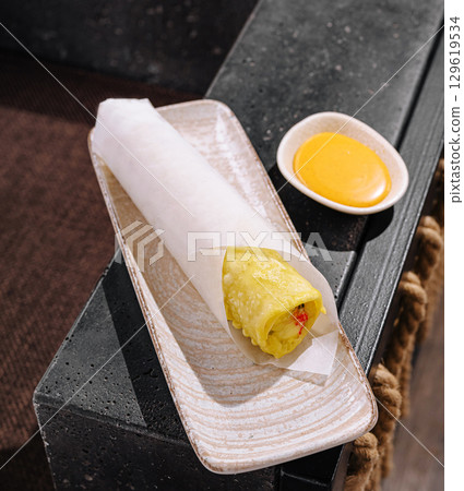 Delicious rolled crepe served with flavorful dipping sauce on a plate 129619534
