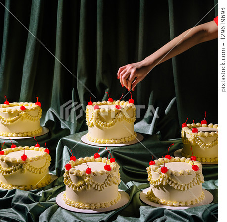Bakers decorate multiple cakes with cherries in a studio setting 129619693