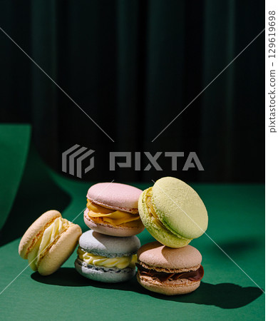 Colorful macarons stacked on a green surface with a dark backdrop 129619698
